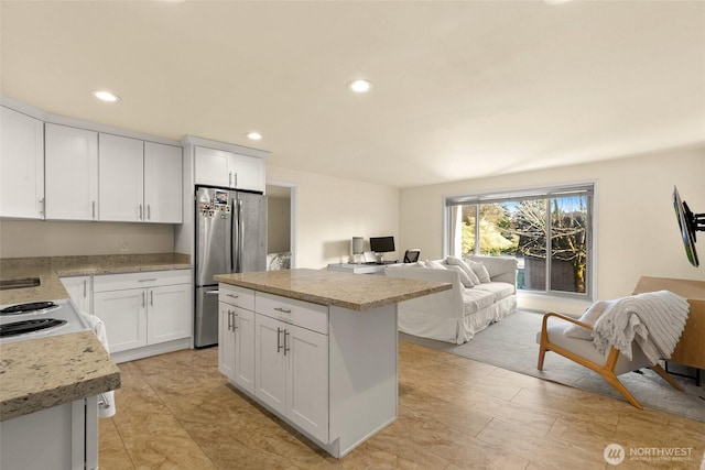kitchen featuring a kitchen island, electric range, white cabinets, freestanding refrigerator, and open floor plan