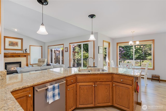 kitchen with dishwasher, a sink, light stone counters, light wood finished floors, and a tiled fireplace