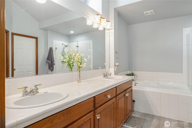 full bathroom with a stall shower, double vanity, a bath, and wood finished floors