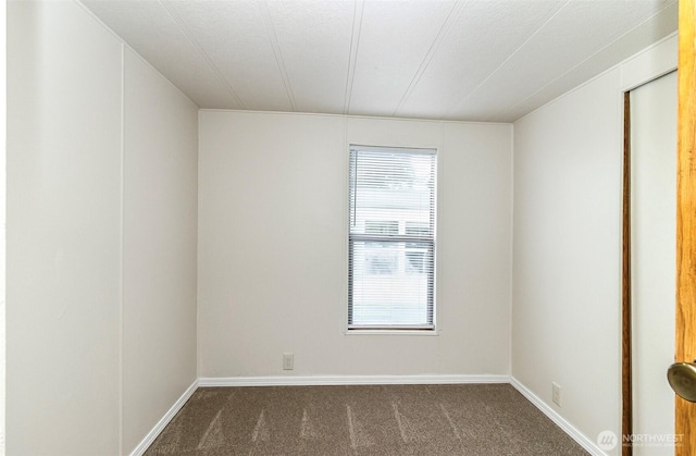 empty room featuring dark colored carpet and baseboards