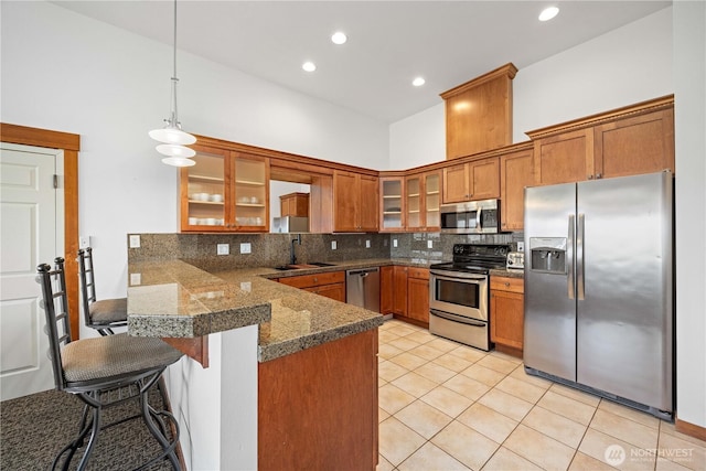 kitchen featuring a sink, tile countertops, brown cabinets, stainless steel appliances, and a peninsula