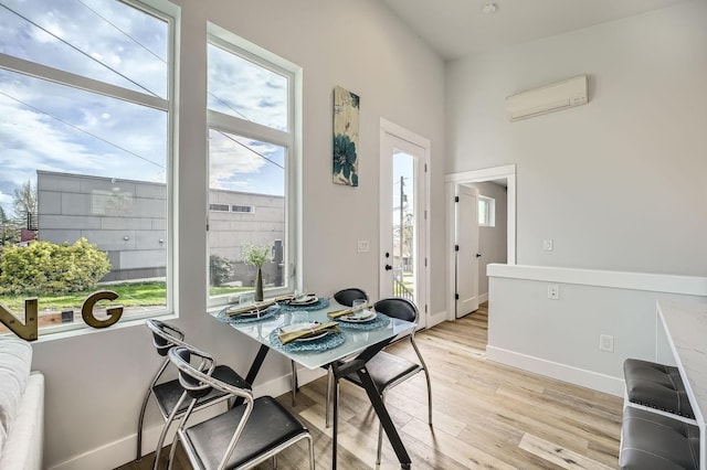 dining room featuring light wood-style floors, a wall mounted AC, and baseboards