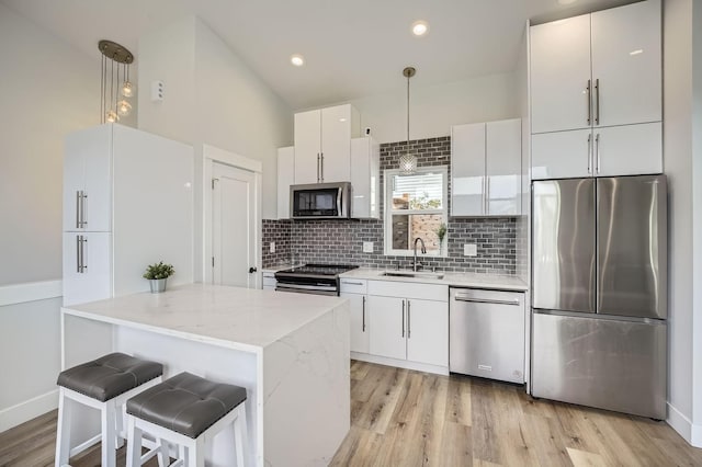 kitchen with light wood-style flooring, a sink, white cabinetry, stainless steel appliances, and decorative backsplash