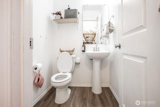 half bath featuring baseboards, a sink, wood finished floors, and toilet