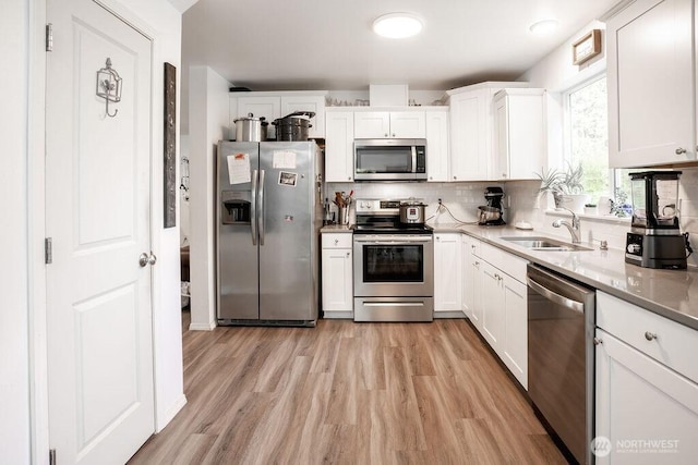 kitchen featuring appliances with stainless steel finishes, tasteful backsplash, a sink, white cabinets, and light wood-style flooring