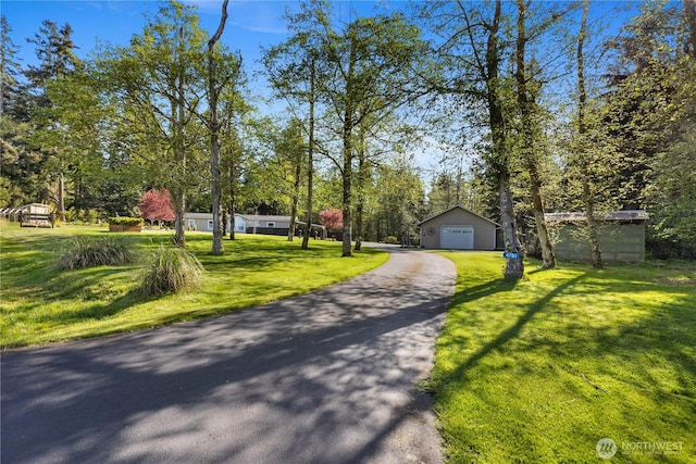 view of front of property featuring a front lawn, aphalt driveway, a detached garage, and an outdoor structure