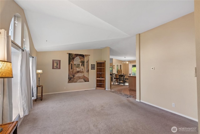 unfurnished living room with a chandelier, carpet floors, baseboards, and lofted ceiling