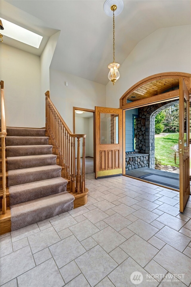 entrance foyer with stairway, an inviting chandelier, and lofted ceiling with skylight