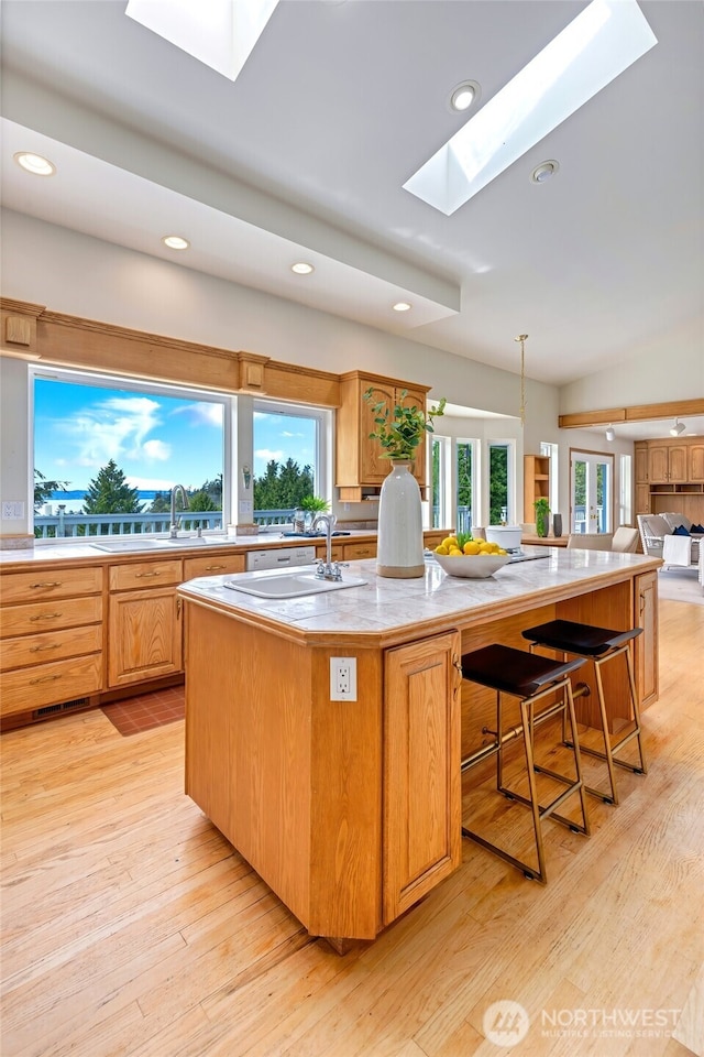 kitchen featuring light countertops, an island with sink, light wood-type flooring, recessed lighting, and a skylight