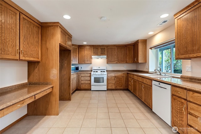 kitchen with white appliances, brown cabinetry, visible vents, under cabinet range hood, and a sink