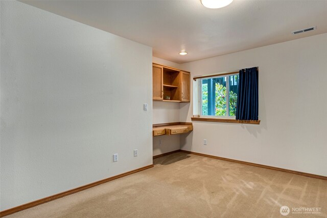 unfurnished room featuring baseboards, light colored carpet, built in study area, and visible vents