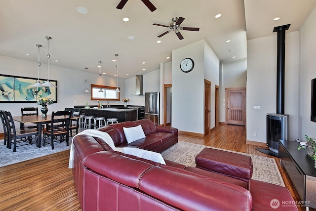 living area with recessed lighting, light wood finished floors, a wood stove, baseboards, and ceiling fan