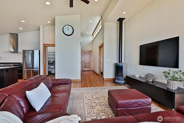living area featuring light wood-type flooring, recessed lighting, a high ceiling, ceiling fan, and a wood stove