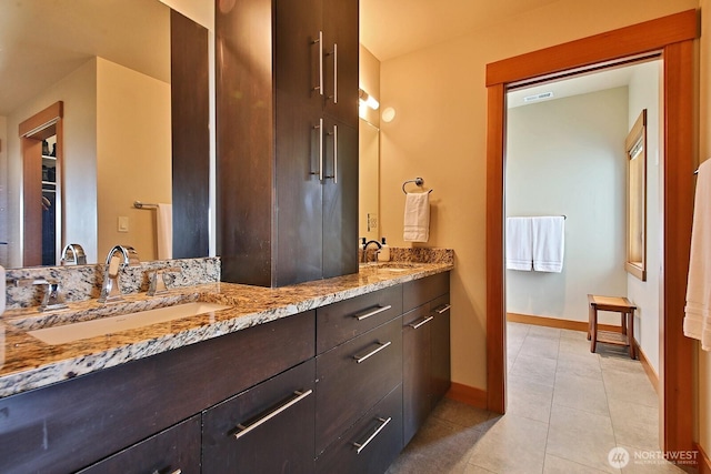 bathroom featuring baseboards, tile patterned floors, a sink, and double vanity