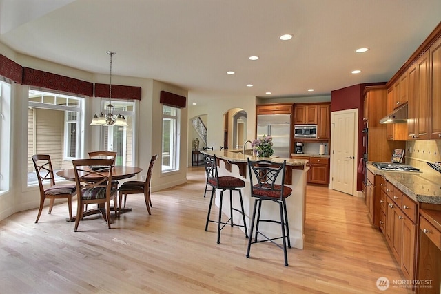 kitchen with built in appliances, a kitchen bar, light wood finished floors, brown cabinets, and recessed lighting