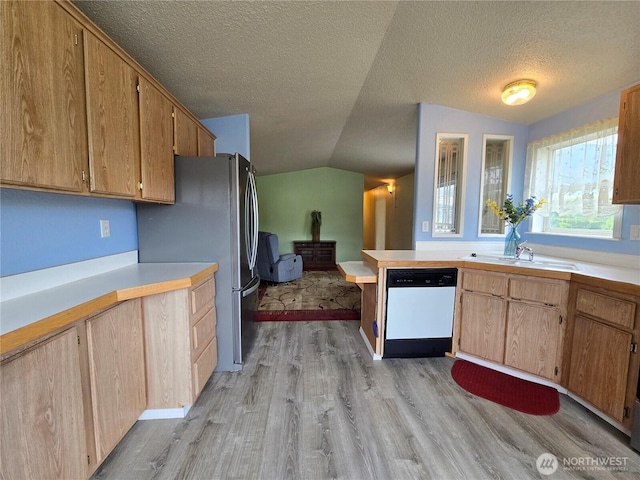 kitchen with white dishwasher, light wood-style floors, light countertops, and vaulted ceiling