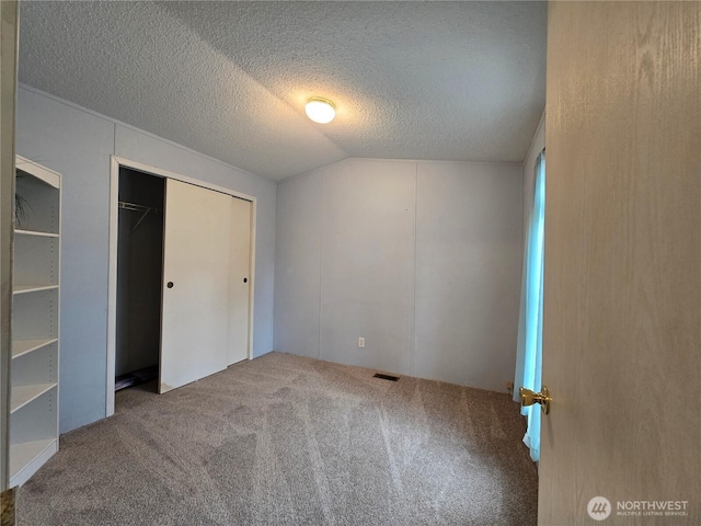 unfurnished bedroom featuring a closet, a textured ceiling, carpet floors, visible vents, and lofted ceiling