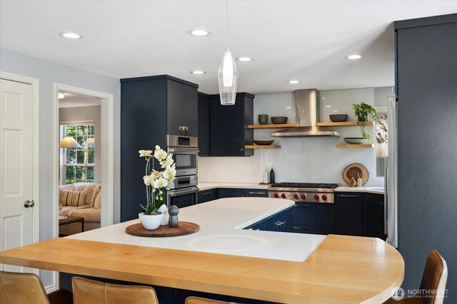 kitchen with open shelves, a kitchen island, wall chimney range hood, light countertops, and stainless steel appliances