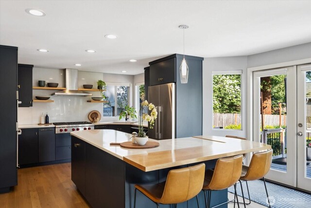 kitchen with a breakfast bar area, island exhaust hood, pendant lighting, appliances with stainless steel finishes, and open shelves