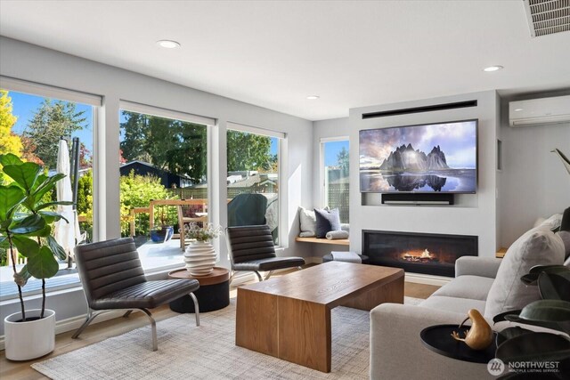 interior space with light wood-style floors, visible vents, a wall mounted AC, a glass covered fireplace, and recessed lighting