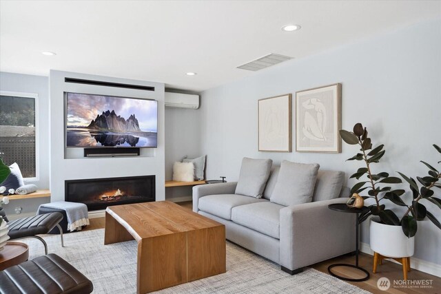 living area featuring light wood finished floors, a glass covered fireplace, recessed lighting, a wall unit AC, and visible vents