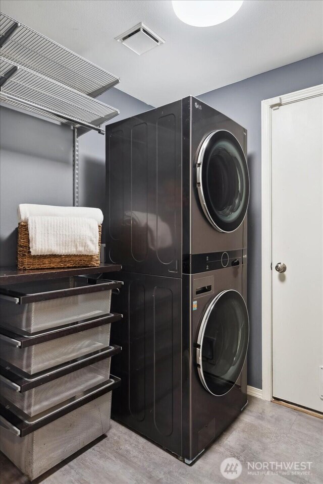 clothes washing area with laundry area, stacked washer and dryer, and visible vents