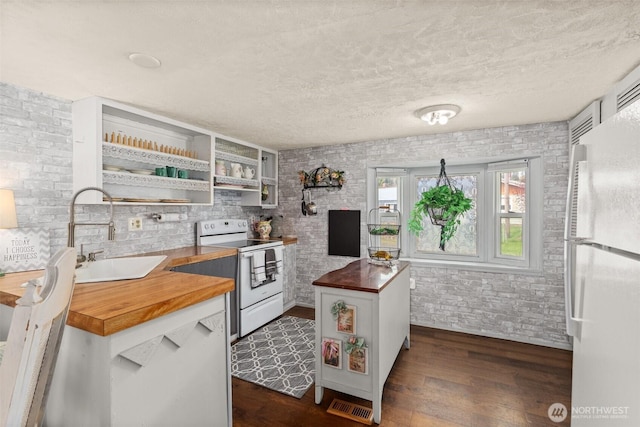 kitchen with white appliances, butcher block counters, visible vents, dark wood-style flooring, and a sink