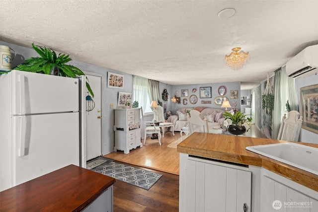 kitchen featuring freestanding refrigerator, dark wood finished floors, a textured ceiling, a wall mounted AC, and butcher block countertops