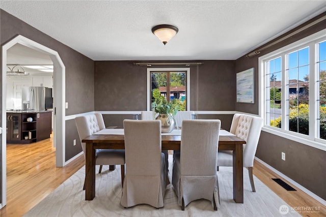 dining space featuring a textured ceiling, visible vents, a wealth of natural light, and light wood-type flooring