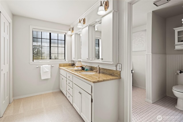 bathroom with double vanity, a sink, wainscoting, and toilet