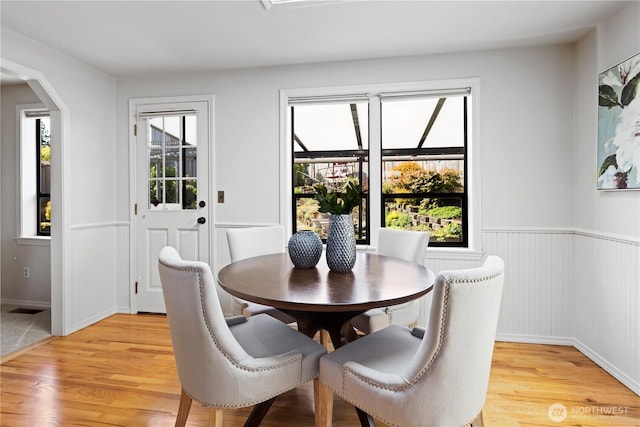 dining space featuring arched walkways, wainscoting, and light wood-style flooring