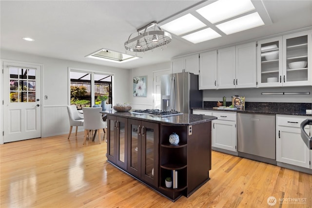 kitchen with open shelves, glass insert cabinets, light wood-type flooring, dark stone counters, and appliances with stainless steel finishes