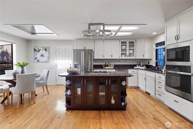 kitchen featuring a center island, a sink, glass insert cabinets, stainless steel appliances, and white cabinetry