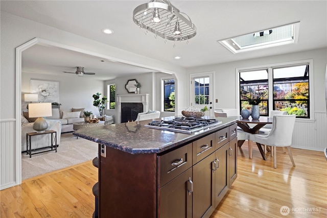 kitchen featuring a kitchen island, a skylight, a high end fireplace, stainless steel gas cooktop, and light wood-style flooring