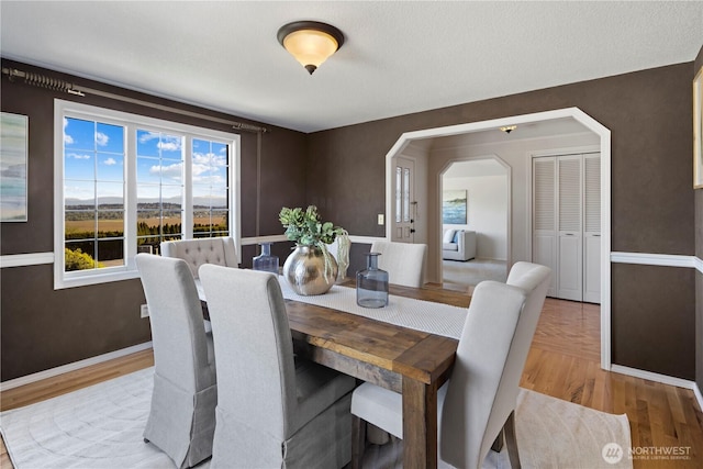 dining space with arched walkways, baseboards, and wood finished floors