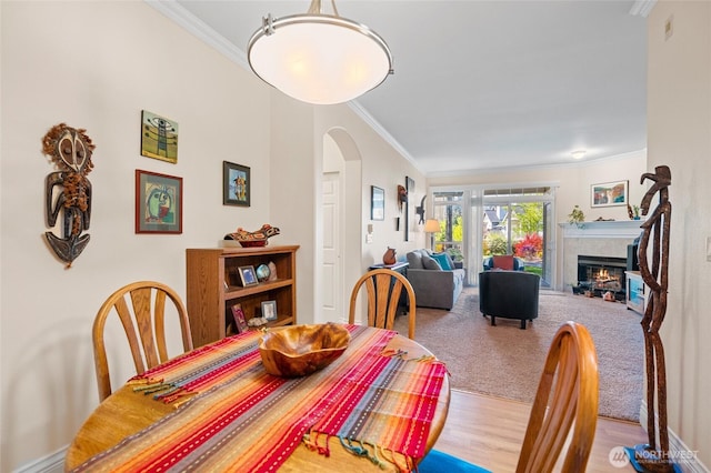 dining area with a tiled fireplace, arched walkways, ornamental molding, and wood finished floors