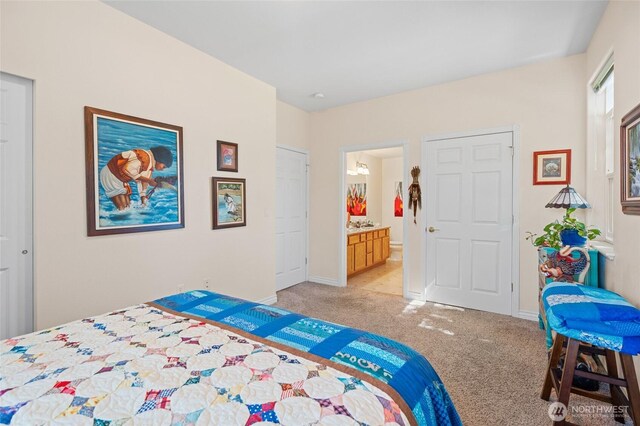 bedroom with baseboards, light colored carpet, and ensuite bath