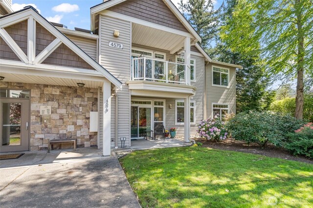 back of house featuring a patio, stone siding, a yard, and a balcony