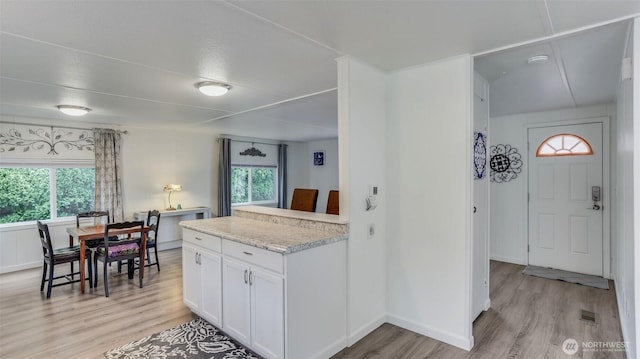 kitchen featuring light wood finished floors, white cabinets, light stone countertops, and baseboards