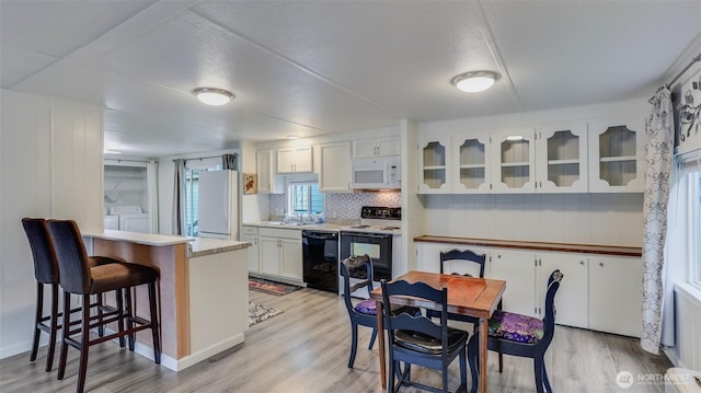 kitchen featuring white appliances, washing machine and dryer, light wood finished floors, white cabinets, and a kitchen bar
