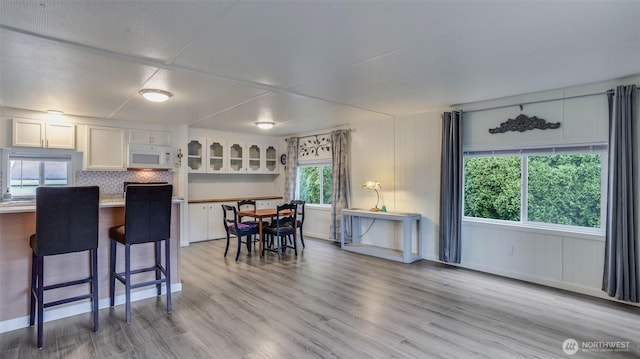 kitchen with white microwave, a kitchen bar, white cabinets, light wood-style floors, and tasteful backsplash