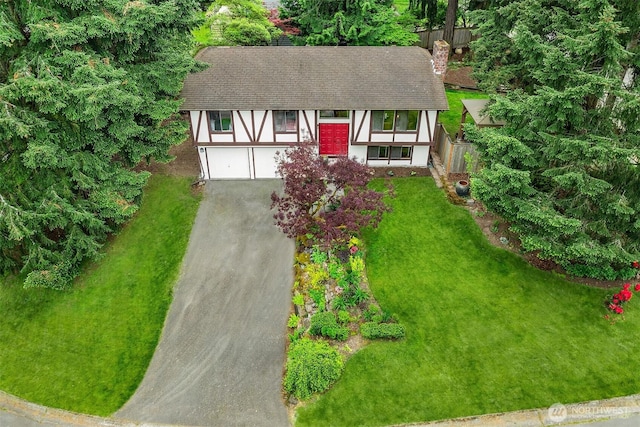 view of front of house featuring a shingled roof, asphalt driveway, an attached garage, a chimney, and a front yard