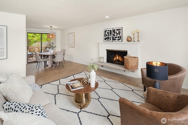 living room featuring wood finished floors, a fireplace, baseboards, a textured ceiling, and recessed lighting