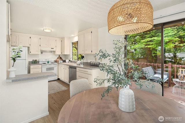 kitchen with white appliances, under cabinet range hood, wood finished floors, white cabinets, and a sink