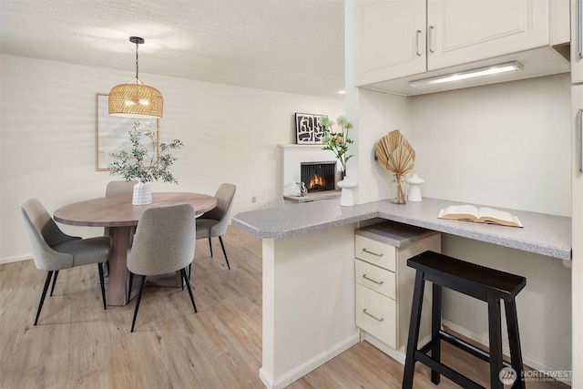 dining space featuring light wood finished floors, a fireplace, a textured ceiling, and baseboards