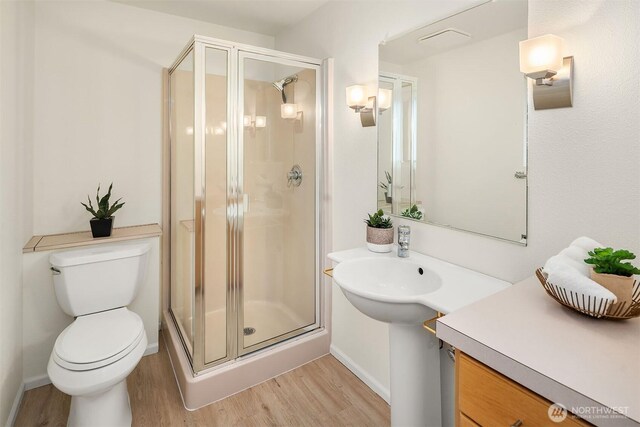 bathroom featuring wood finished floors, a shower stall, toilet, and baseboards