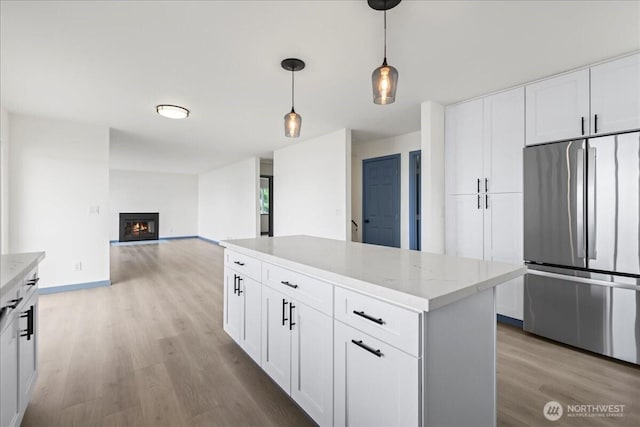 9360 SE Southworth Dr, Port Orchard, WA 98366 - kitchen with pendant lighting, light wood-type flooring, stainless steel refrigerator, a glass covered fireplace, and white cabinets