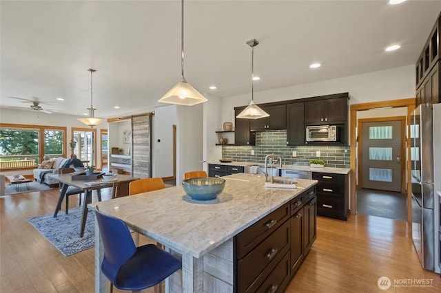 8996 Dearborn Ave, Blaine, WA 98230 - kitchen with decorative backsplash, a kitchen island with sink, light wood-type flooring, and decorative light fixtures
