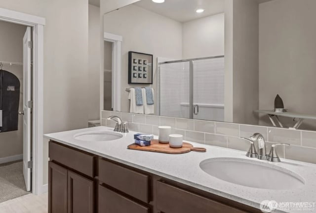 full bathroom with backsplash, double vanity, a shower stall, and a sink