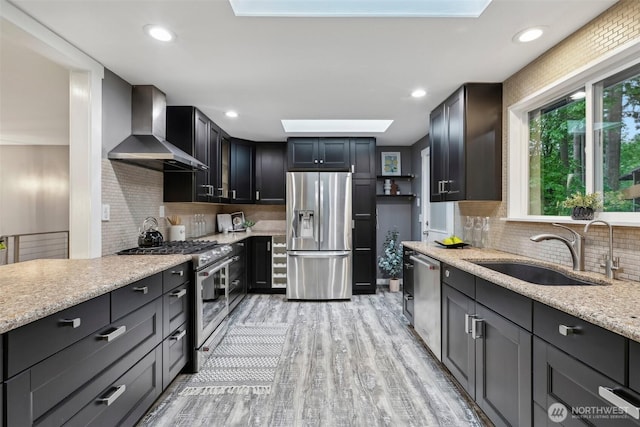 320 SW Forest Dr, Issaquah, WA 98027 - kitchen featuring appliances with stainless steel finishes, wall chimney range hood, a sink, a skylight, and light stone counters
